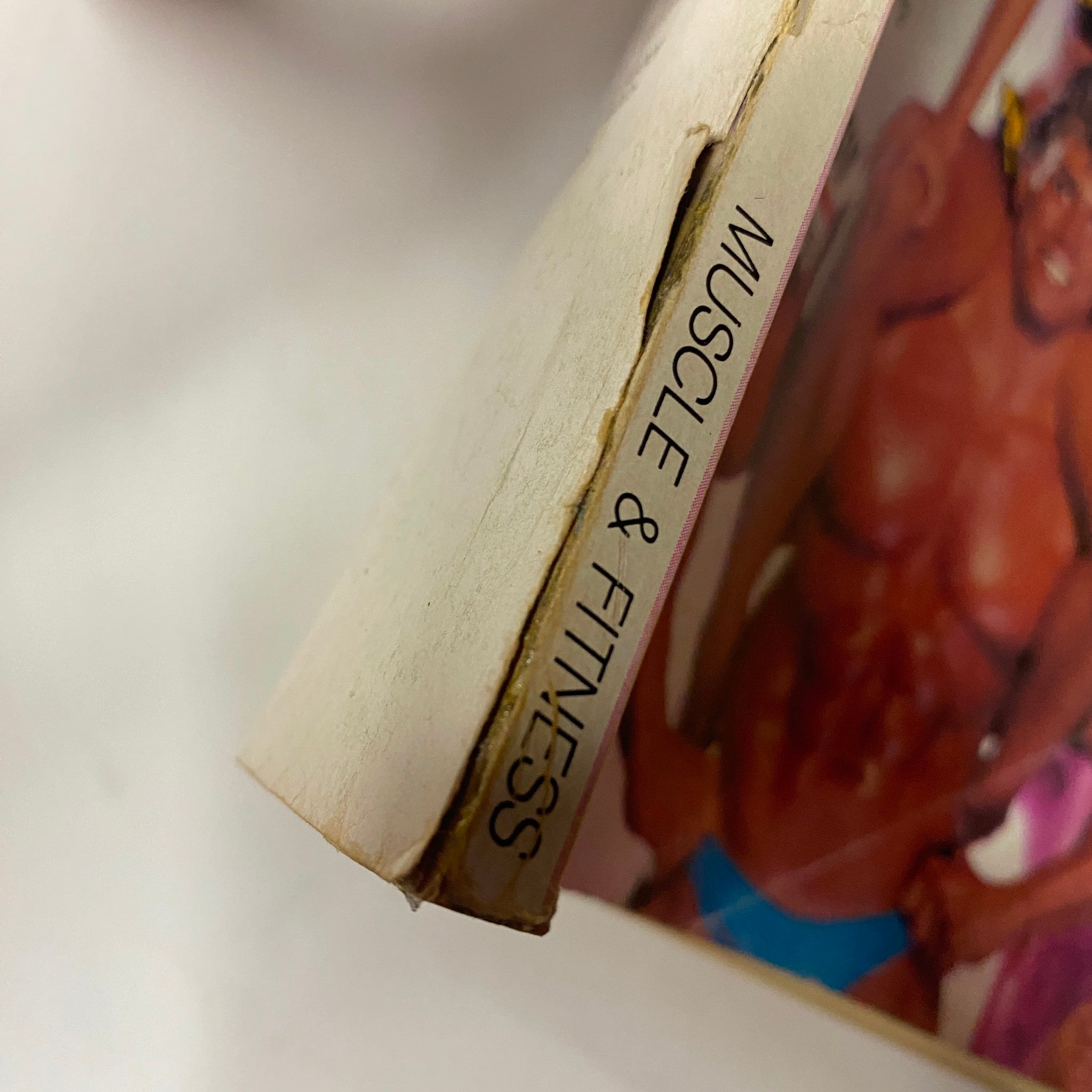 Close-up of the spine of the Muscle & Fitness Magazine July 1984, illustrating its title and signs of aging on the pages.