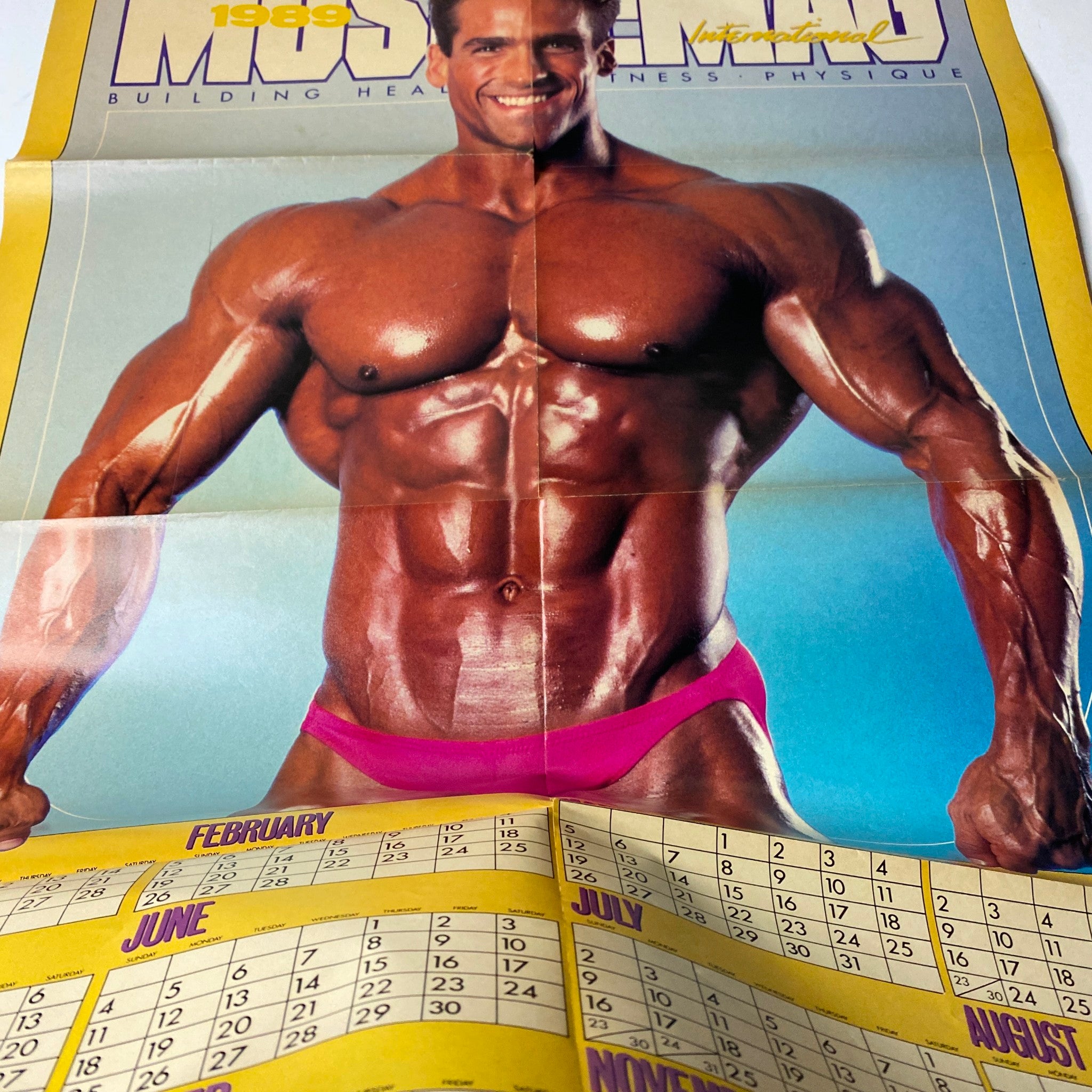 Detached calendar poster from MuscleMag International Magazine November 1988 No. 79 featuring a muscular man in pink posing trunks, illustrating fitness and bodybuilding.