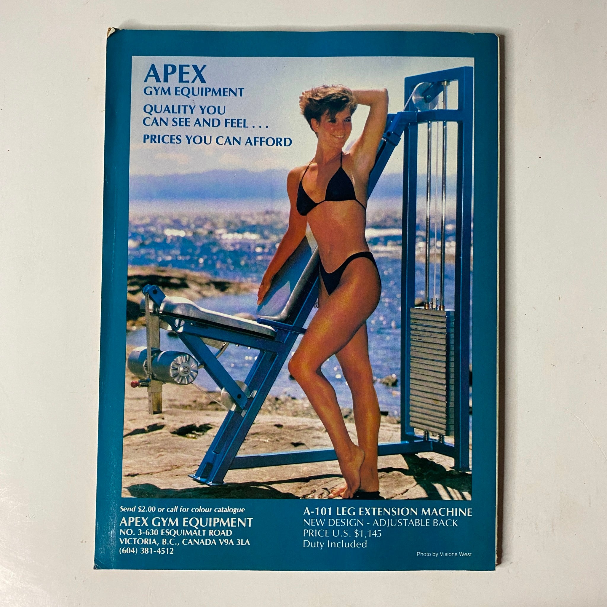 Vintage advertisement for Apex Gym Equipment featuring a model in a bikini next to a leg extension machine. The ad emphasizes quality and affordability, linking to the MuscleMag International Magazine December 1989 issue titled 'MuscleMag International Magazine December 1989 No. 91 Bob Paris, Cory Everson VG'.