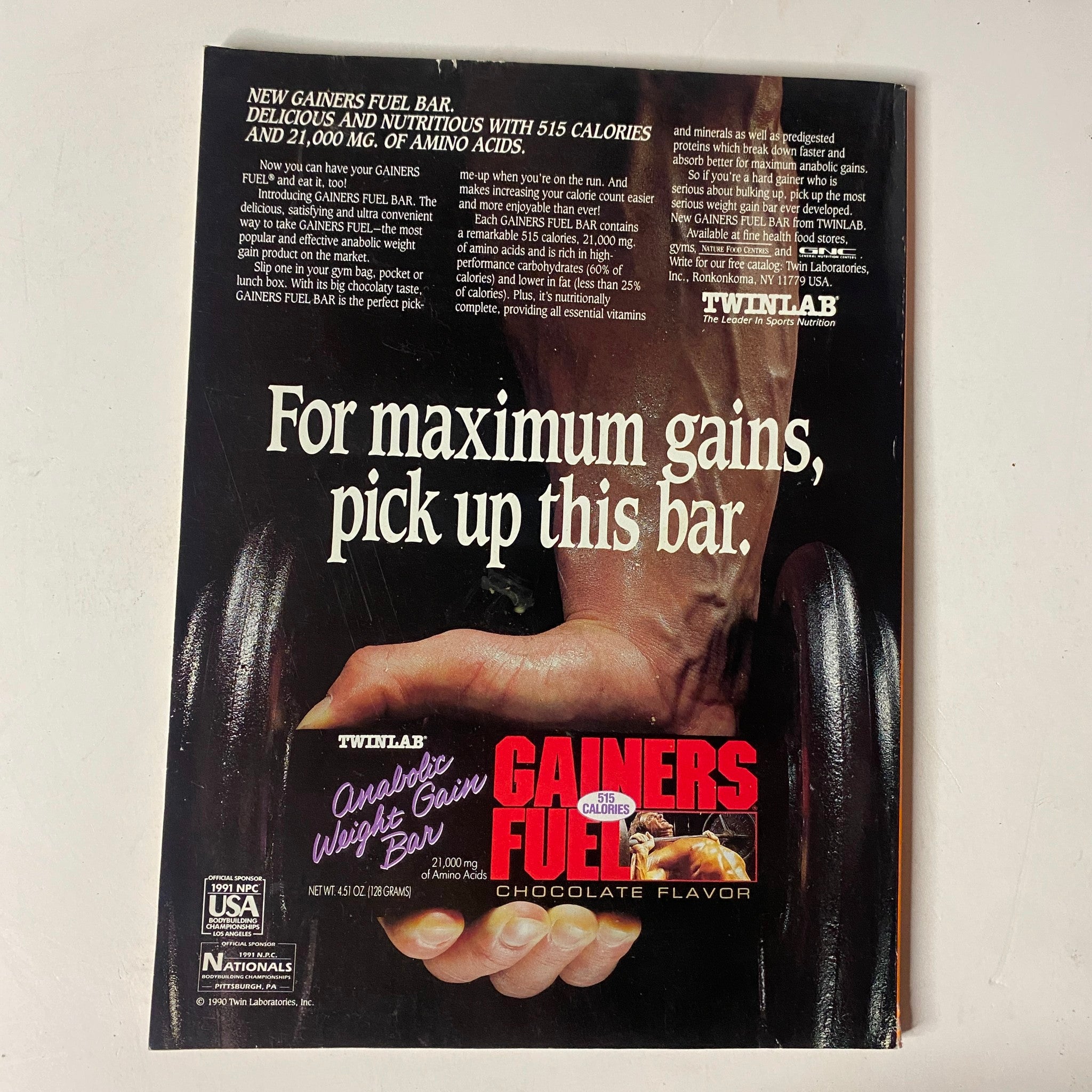 Advertisement for Twinlab Gainors Fuel Bar featured in MuscleMag International Magazine August 1991 No. 110 Jerry Steele. The ad promotes delicious and nutritious weight gain with 515 calories and branched-chain amino acids, encouraging readers to pick up the chocolate-flavored bar.