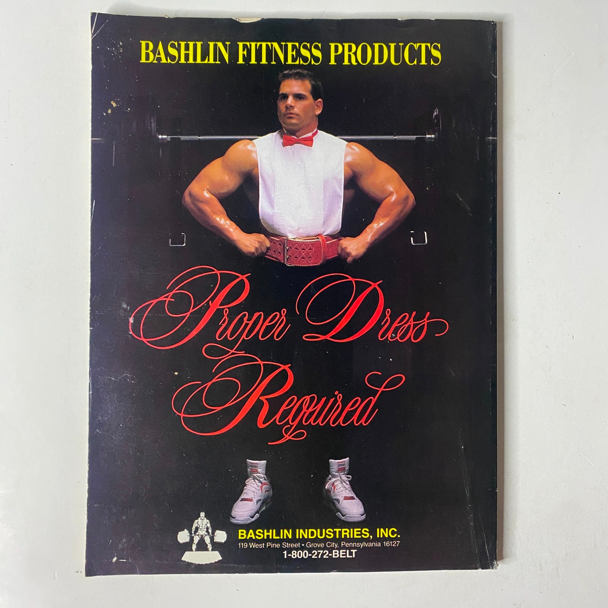 MuscleMag International Magazine January 1991 No. 104 includes an advertisement for Bashlin Fitness Products showcasing the 'Proper Dress Required' promotional design.