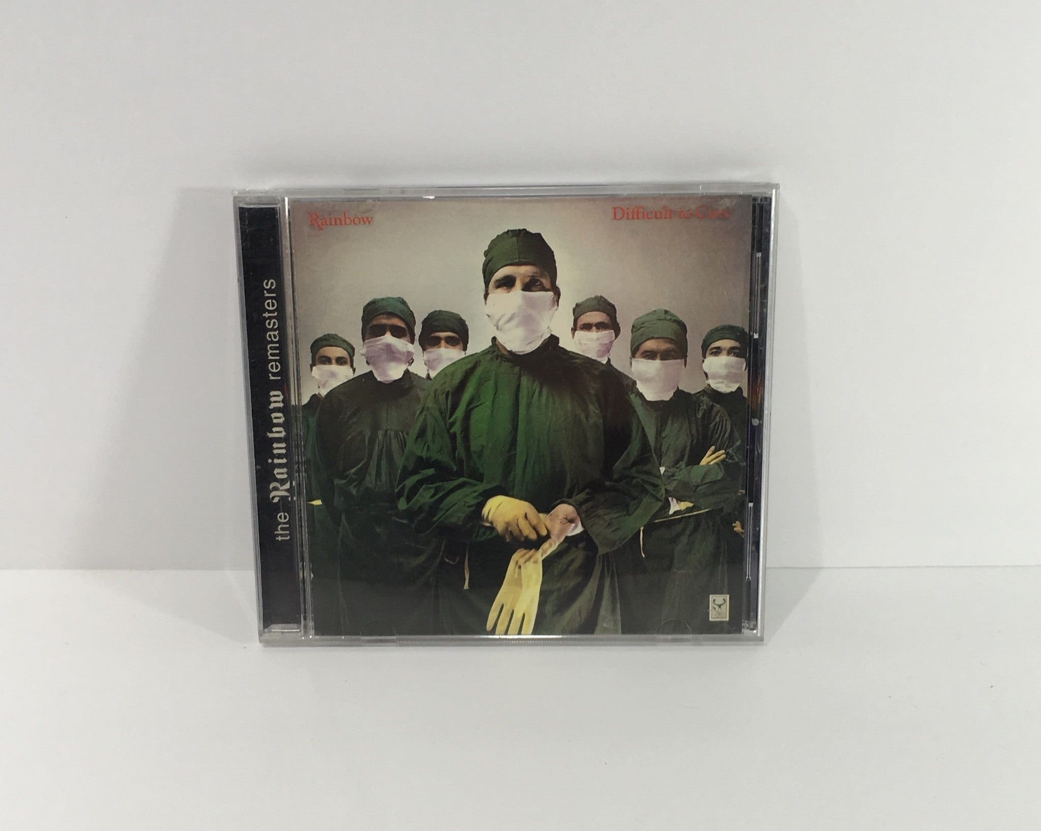 Rainbow Difficult To Cure Remasters Music Audio CD featuring a striking cover image of masked figures in surgical attire, conveying a dramatic aesthetic.