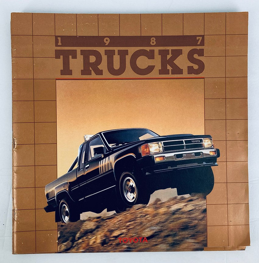 1987 Toyota Trucks Dealer Showroom Sales Brochure Guide Catalog featuring a black Toyota truck driving on rugged terrain with a bold '1987 TRUCKS' title on the cover.
